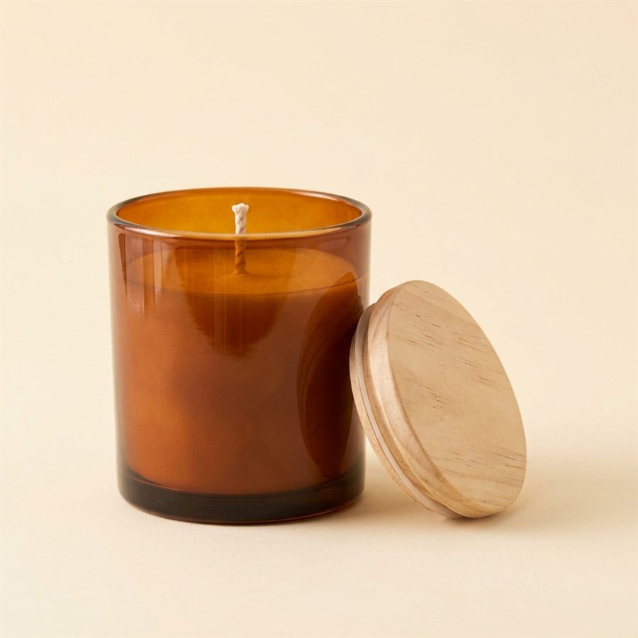 An amber glass jar candle with its wooden lid beside it