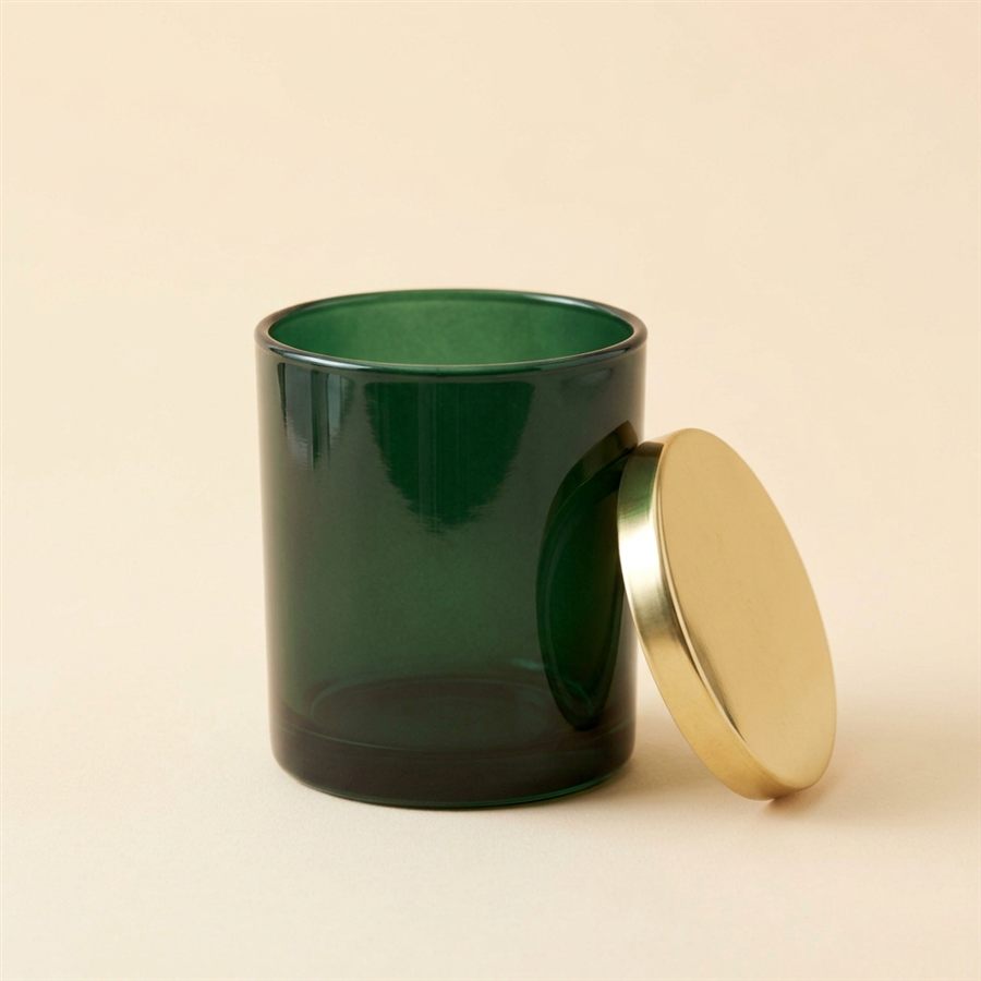 A dark green glass jar candle with a brass lid beside it