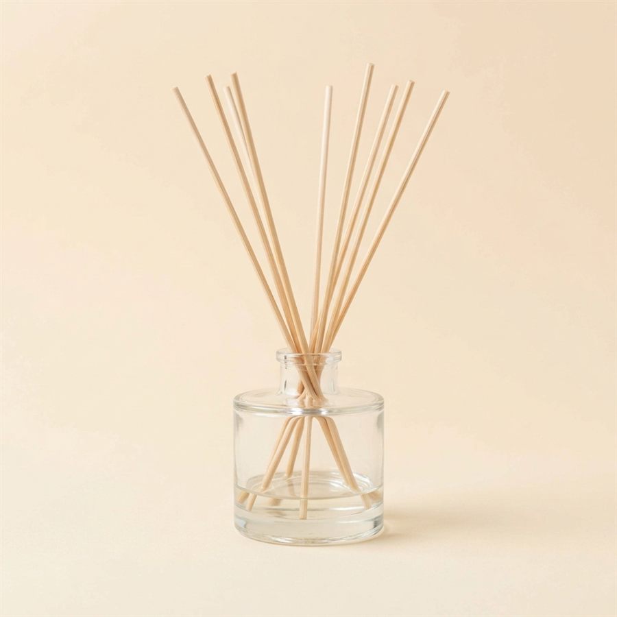 A clear glass reed diffuser bottle with thin wooden reeds